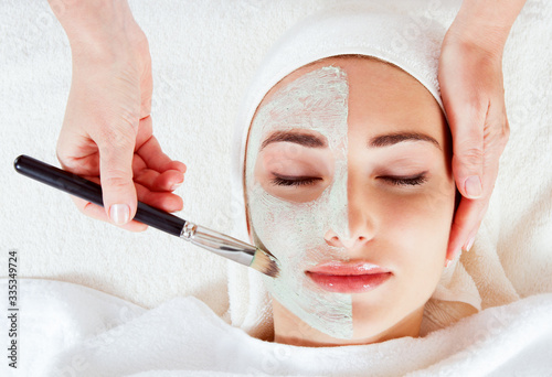 Spa Woman applying Facial clay Mask. Beauty Treatments. Close-up portrait of beautiful girl with a towel on her head applying facial mask.