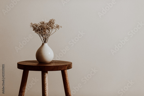 White ceramic vase on a natural brown wooden stool with white dried flowers in an empty room photo