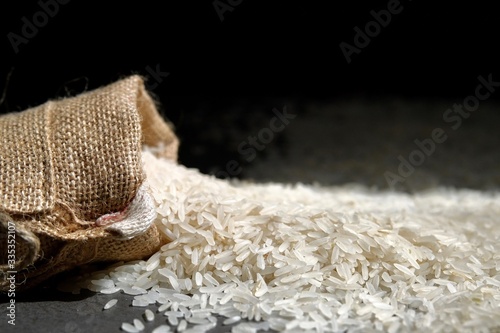 Composition with white rice. Long grain rice scattered around a bag of coarse natural fabric. 