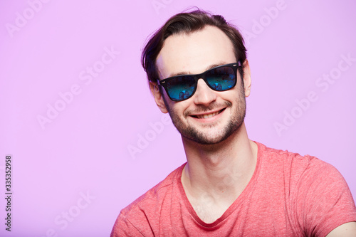 Closeup portrait of awesome hipster wearing sunglasses with intense look at camera. Headshot over pink studio background.