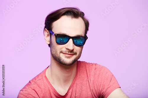 Closeup portrait of awesome hipster wearing sunglasses with intense look at camera. Headshot over pink studio background. © sarymsakov.com