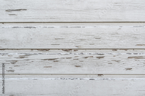 Wooden wall with bits and pieces of paint peeling off in a faded white color.