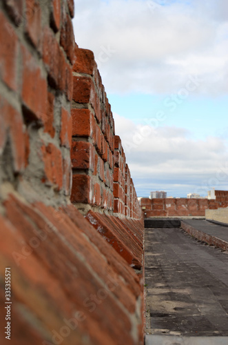 a wall of red brick goes into the distance against the sky with clouds photo