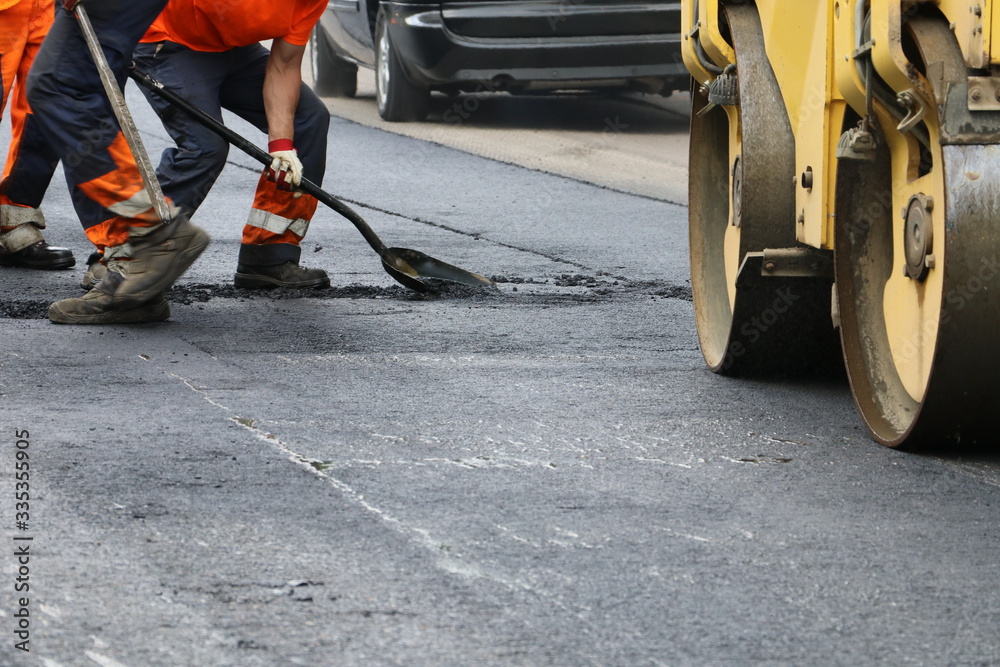 Fototapeta premium Worker using tool to smooth asphalt on driveway. Road repairing.