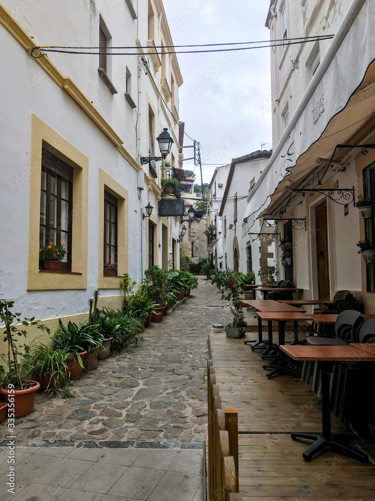Historic, narrow spanish street with a restaurant terrace, guesthouse, flowers, and a street lamp