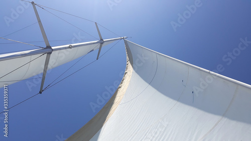 Sailing under the blue sky on a sunny day. Sails of a sailing yacht in the wind. Close up of yacht mast and sail on sky background. Sailing boat part.
