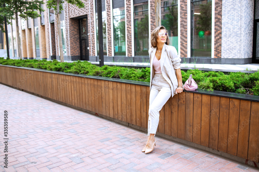 Fototapeta premium Successful business woman in cityscape background. Stylish lady outdoor with handbag. Fahionable female manager leaves her modern office. Street fashion. ..