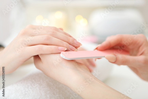 Closeup shot of a woman in a nail salon getting a manicure by a cosmetologist with a nail file. Woman gets a manicure of nails. Beautician puts nails on the client.
 photo