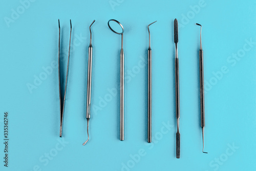Set of metal dentist tools and equipment isolated on a blue background. Steel made mouth mirror, periodontal explorer scaler, tweezers and other instruments. Dental health and teeth care concept