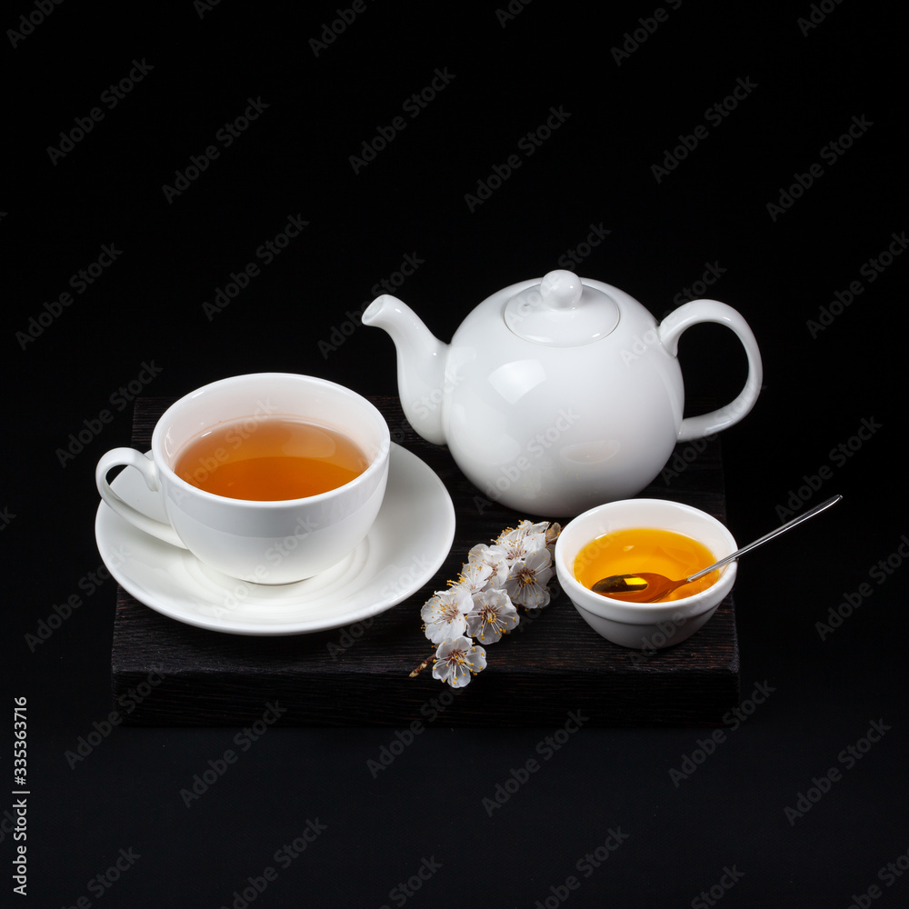 White porcelain tea set and a blooming cherry branch on a black background White porcelain tea set and a blooming cherry branch on a black background