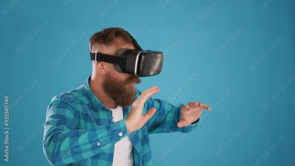 portrait of Caucasian man with beard and mustache in blue shirt, touch something with modern 3D vr augmented reality glasses, on blue background close-up 4K frame portrait of Caucasian man with beard and mustache in blue shirt, touch something with modern 3D vr augmented reality glasses, on blue background close-up 4K frame