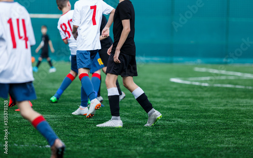 Boys in white and blue sportswear plays football on field, dribbles ball. Young soccer players with ball on green grass. Training, football, active lifestyle for kids concept © Natali