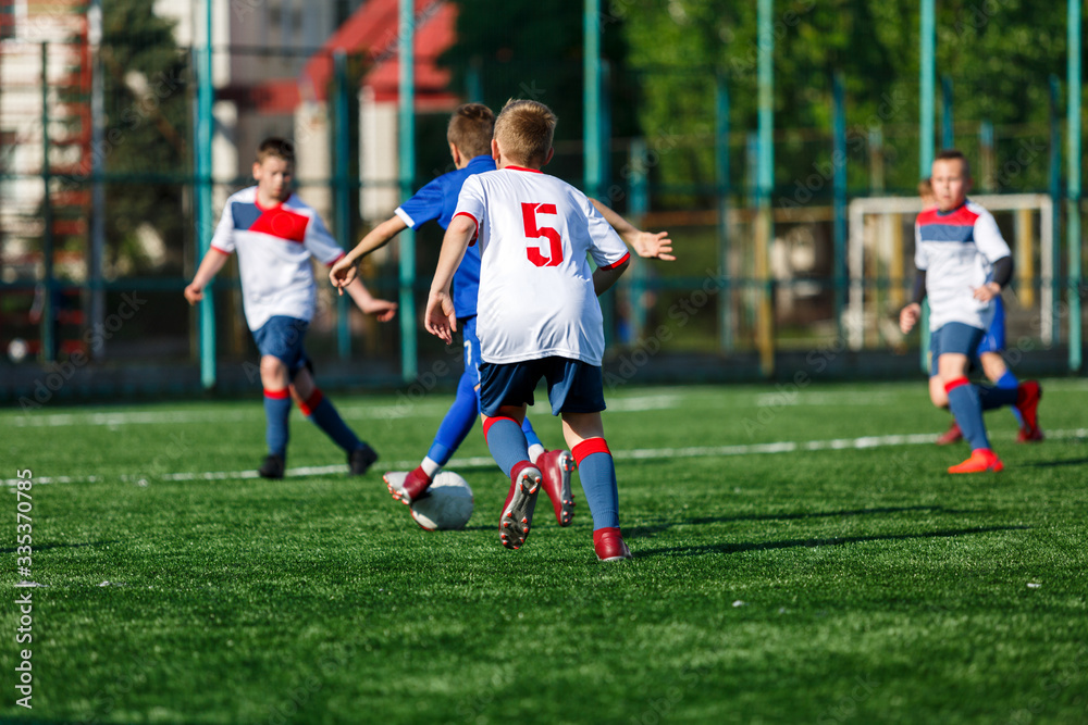 Boys in white and blue sportswear plays football on field, dribbles ball. Young soccer players with ball on green grass. Training, football, active lifestyle for kids concept Boys in white and blue sportswear plays football on field, dribbles ball. Young soccer players with ball on green grass. Training, football, active lifestyle for kids concept