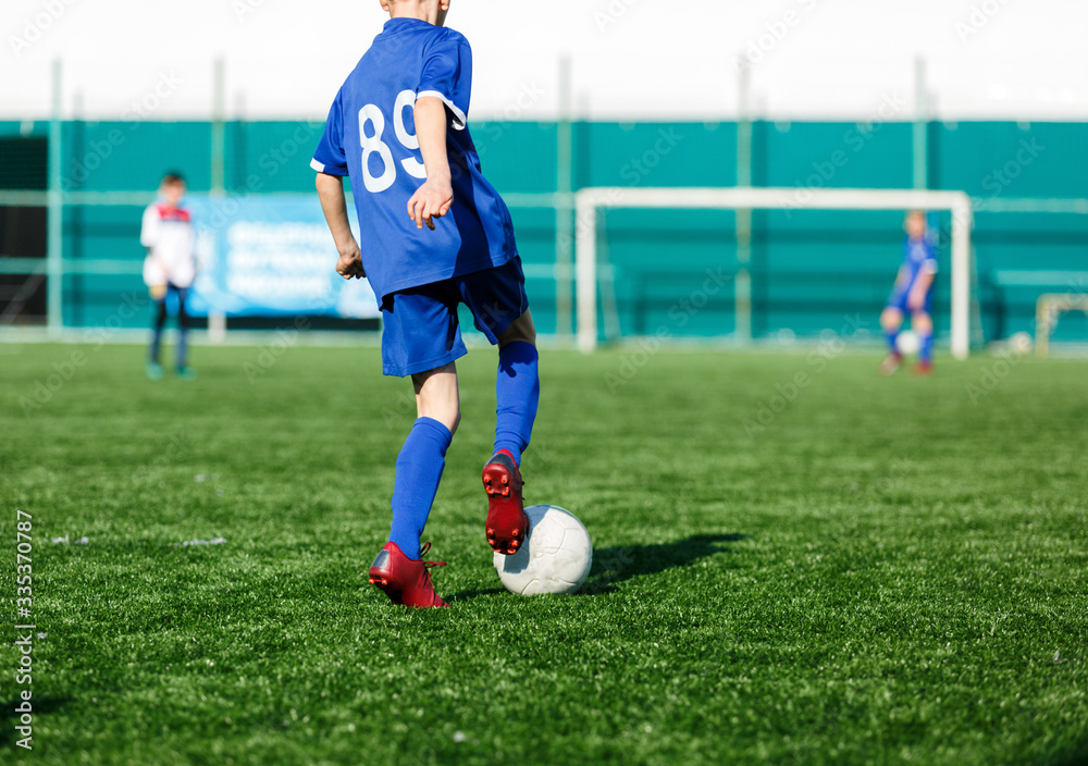 Boys in white and blue sportswear plays football on field, dribbles ball. Young soccer players with ball on green grass. Training, football, active lifestyle for kids concept Boys in white and blue sportswear plays football on field, dribbles ball. Young soccer players with ball on green grass. Training, football, active lifestyle for kids concept
