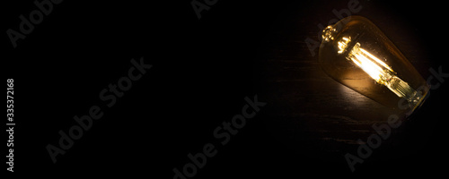 Invention, ideas and leadership concept; Close up glowing lighting bulb on dark black background. Panoramic aspect ratio for copy space. 