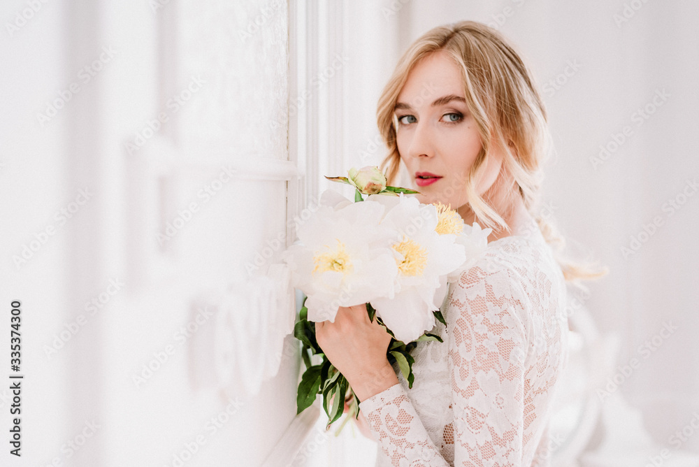 Beautiful bride in a white laced dress and wedding bouquet  is preparing for wedding ceremony in hotel room. Bride getting ready. Artwork