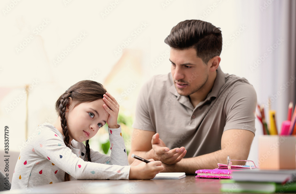 Father scolding his daughter while helping with homework at table indoors Father scolding his daughter while helping with homework at table indoors