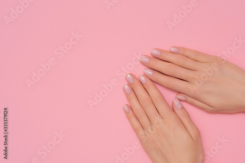 Female hand with orchid flower isolated on pink background. French, delicate manicure.