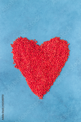 Red lentils scattered on the surface in the form of a heart. Blue background