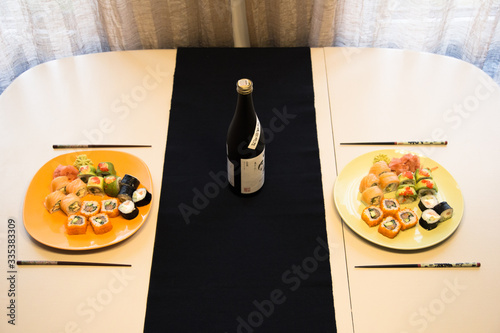 A table for two with a sushi maki set and a bottle of sake in a minimalist style and warm colors.