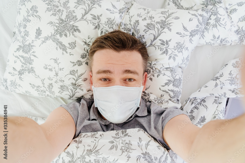 masked man lies at home in bed and taking a selfie