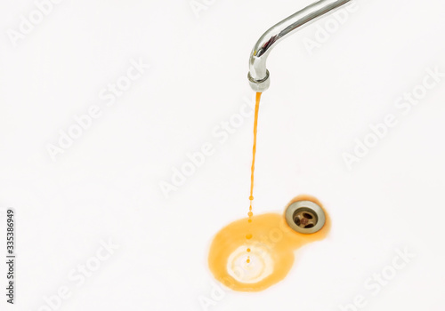 Rusty or dirty water flows from a faucet into a white bathtub or sink 