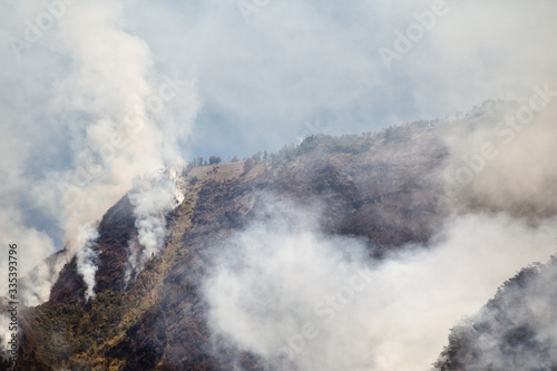 fire in mountain forest. aerial view forest fire and smoke on slopes hills. wild fire in mountains in tropical forest, Java Indonesia. natural disaster fire in Southeast Asia