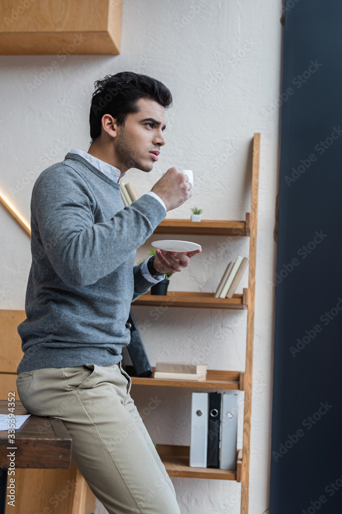 Selective focus of thoughtful businessman with saucer and cup of coffee in office Selective focus of thoughtful businessman with saucer and cup of coffee in office