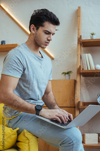 Concentrated freelancer working with laptop on sofa in living room