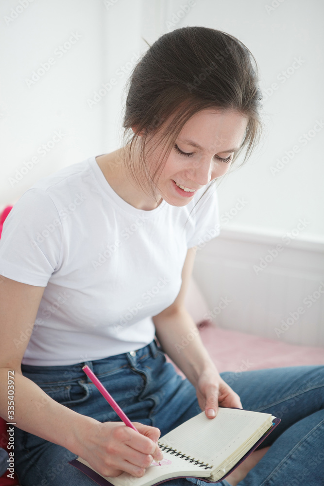 Young woman with notebook sitting on the bed. Peaceful atmosphere. Woman stay home during a quarantine. Home concept. Self isolation. Young woman with notebook sitting on the bed. Peaceful atmosphere. Woman stay home during a quarantine. Home concept. Self isolation.