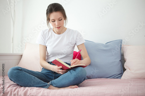 Young woman with notebook sitting on the bed. Peaceful atmosphere. Woman stay home during a quarantine. Home concept. Self isolation.
