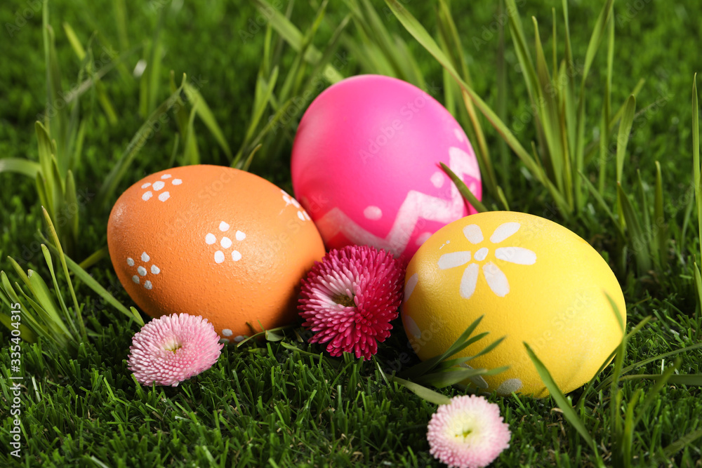 Colorful Easter eggs and daisy flowers in green grass, closeup Colorful Easter eggs and daisy flowers in green grass, closeup