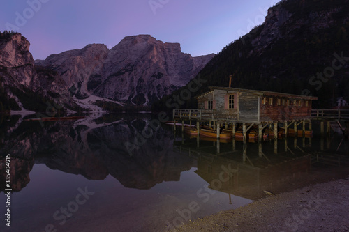 Italian Dolomites, Lago di Braies - evening view of the calm surface of the lake with high banks covered with trees. On the right is a wooden house standing on wooden stilts in the water. © Jana Krizova