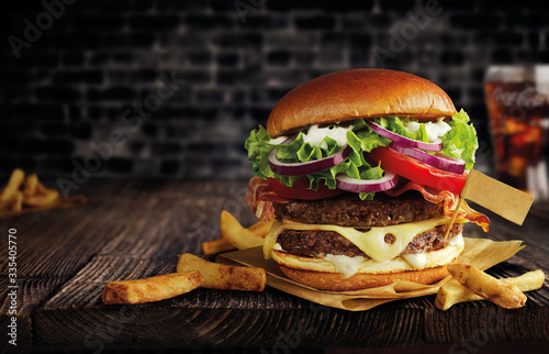 burger with double meat, cheese and french fries on a wooden table, with a flag, black brick wall behind