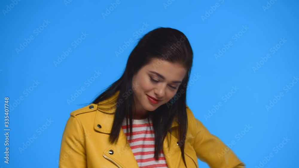 Attractive girl in yellow jacket smiling at camera isolated on blue Attractive girl in yellow jacket smiling at camera isolated on blue