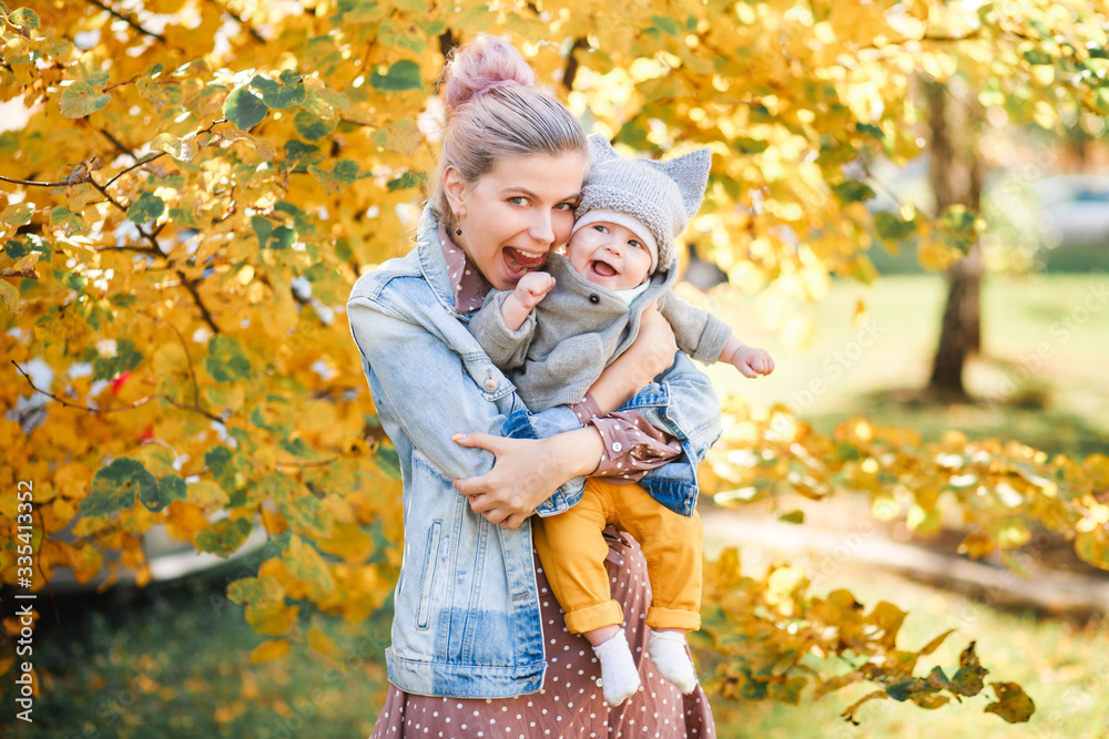 A stylish young mother with a small son in her arms walks in the autumn. A stylish young mother with a small son in her arms walks in the autumn.