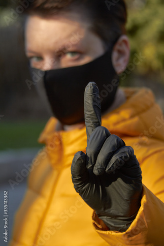 Middle aged european woman in protective black mask makes an warning gesture during coronavirus COVID-19 Epidemic. Sick woman wearing protection during pandemic. photo