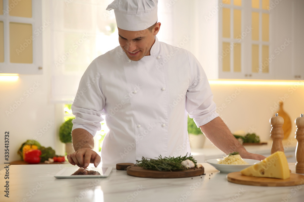 Chef with tablet cooking at table in kitchen Chef with tablet cooking at table in kitchen