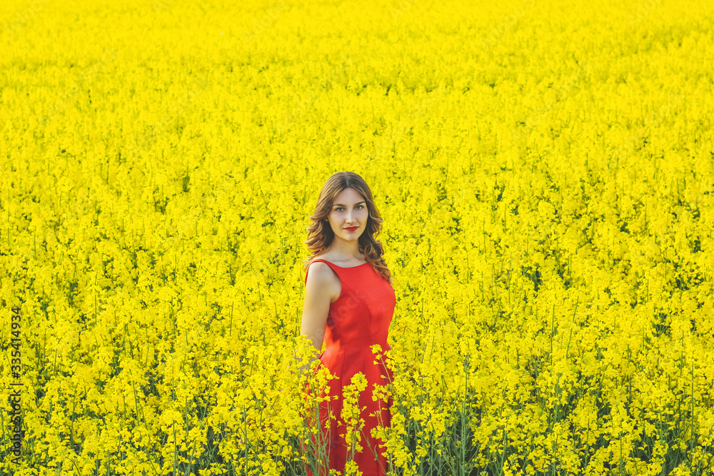 Young beautiful girl in a red dress close up in the middle of the yellow field with the radish flowers closeup Young beautiful girl in a red dress close up in the middle of the yellow field with the radish flowers closeup