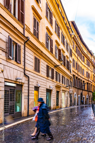 Rome, Italy. Mostly empty narrow cobblestone streets of the Italian city. People walk on road/ lane between ancient Roman buildings. Vintage architecture, closed stores and shops. Rainy day in Europe.