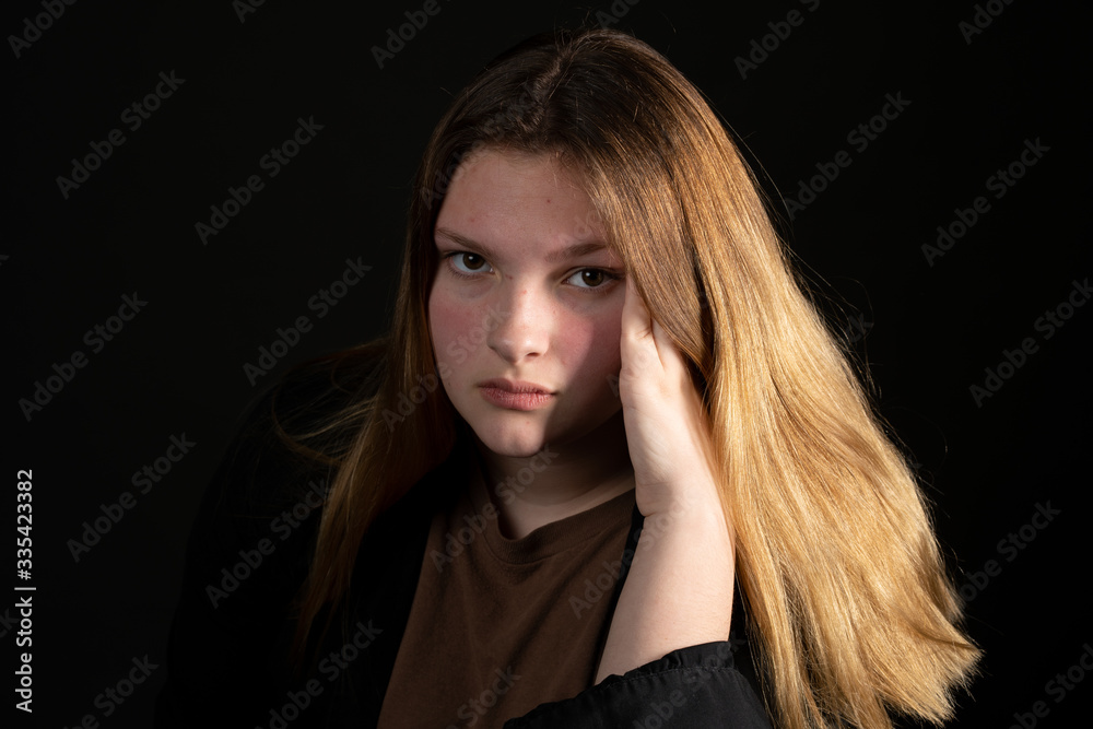 Sad teen girl on a black background with head in hands.