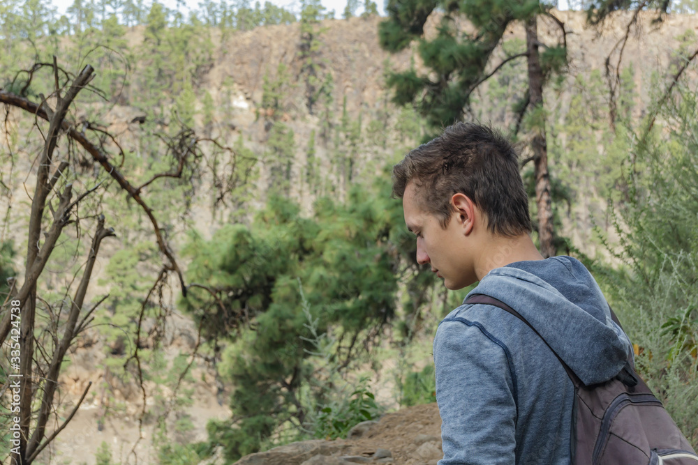 A young man with a backpack travels along a route in the west side of Tenerife. Hiking by the mountain trail surrounded by endemic vegetation pine tree forest and fields of lava rocks. Canary Islands A young man with a backpack travels along a route in the west side of Tenerife. Hiking by the mountain trail surrounded by endemic vegetation pine tree forest and fields of lava rocks. Canary Islands