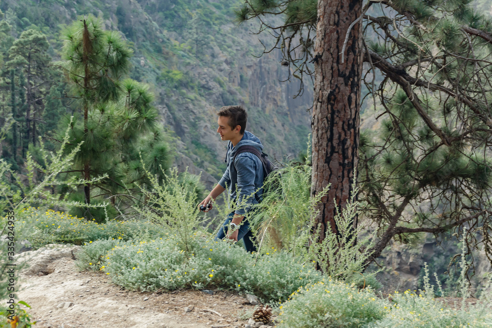 A young man with a backpack travels along a route in the west side of Tenerife. Hiking by the mountain trail surrounded by endemic vegetation pine tree forest and fields of lava rocks. Canary Islands A young man with a backpack travels along a route in the west side of Tenerife. Hiking by the mountain trail surrounded by endemic vegetation pine tree forest and fields of lava rocks. Canary Islands