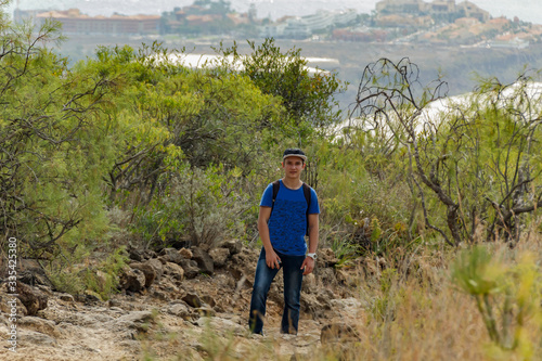 A young man with a backpack travels along a route in the west side of Tenerife. Hiking by the mountain trail surrounded by endemic vegetation and fields of lava rocks. Canary Islands, Spain