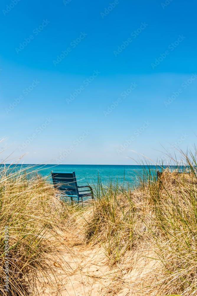Single blue chair, over the sand dunes to the beach and water's edge Single blue chair, over the sand dunes to the beach and water's edge
