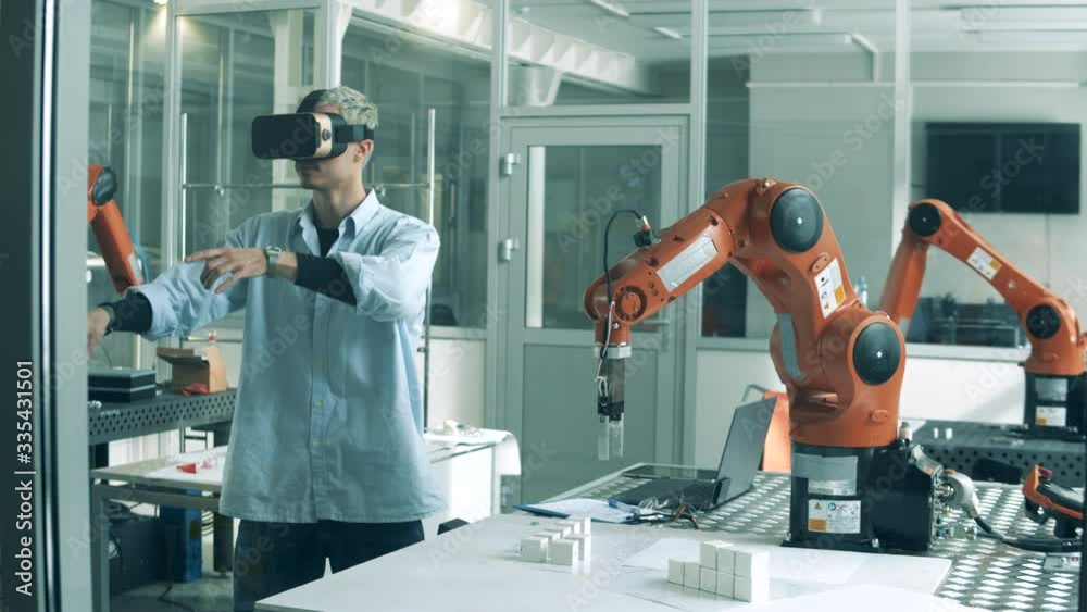 Young scientist is managing a robot through virtual reality. Man wearing VR headset and working with robotic engineering project in lab.