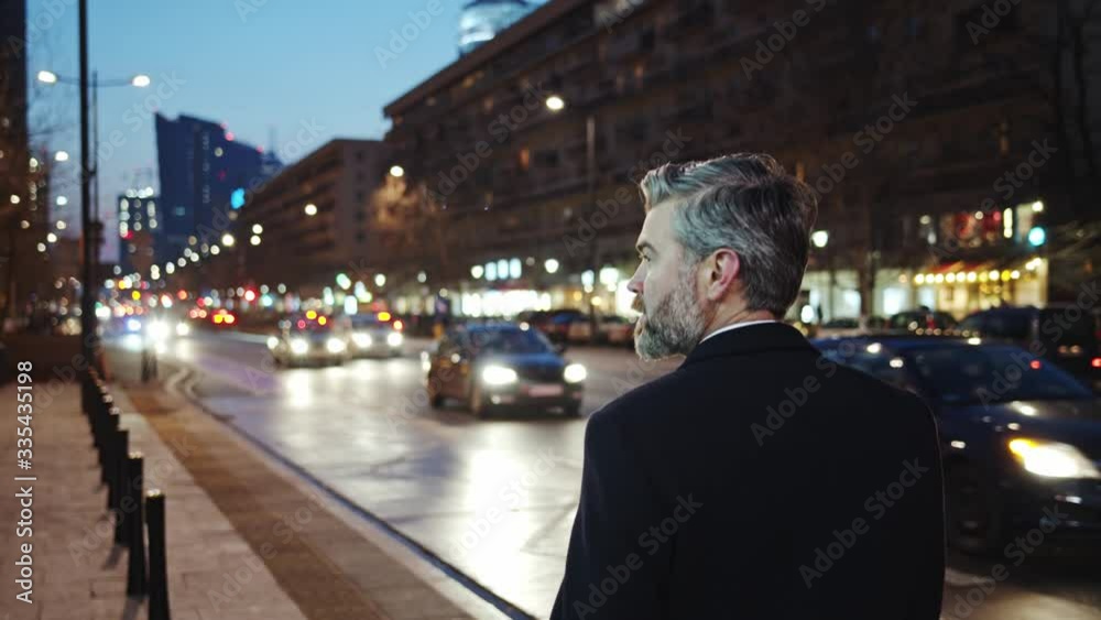 Back of old business caucasian man in suit walks on city street at night admiring architecture travel look around. Business people. Urbanity, modern lifestyle. Back of old business caucasian man in suit walks on city street at night admiring architecture travel look around. Business people. Urbanity, modern lifestyle.