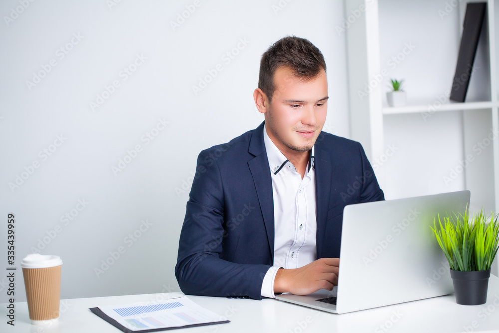 Handsome young worker working in a company office with documents and a laptop Handsome young worker working in a company office with documents and a laptop