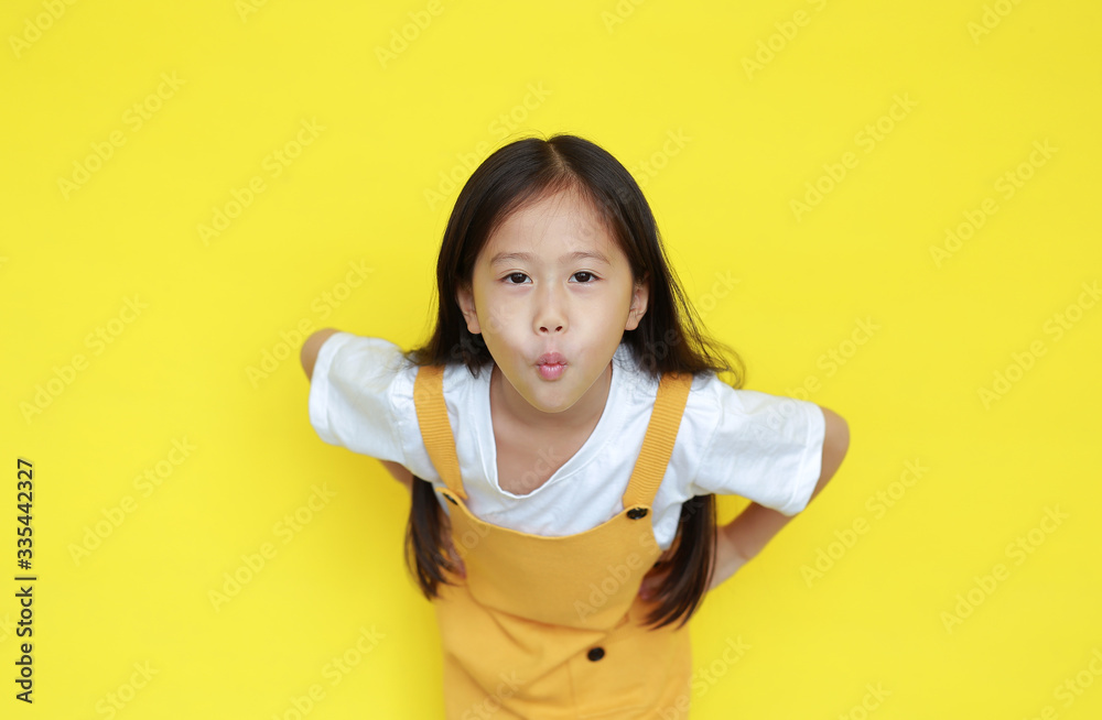 Funny little asian kid girl expression mouth to make a kiss over yellow background. child with love gesture and looking camera Funny little asian kid girl expression mouth to make a kiss over yellow background. child with love gesture and looking camera