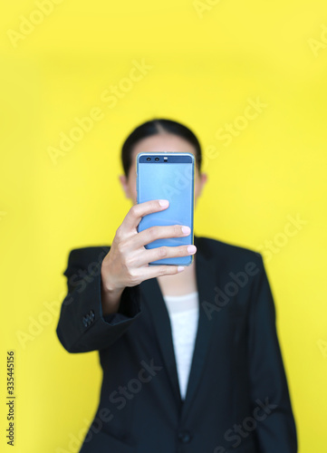 Portrait business woman holding smartphone in her hands isolated on yellow background. Focus at smartphone in her hand.